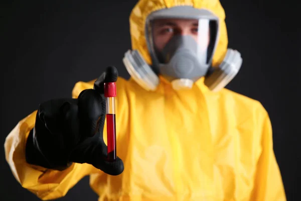 身穿化学防护服的男子手持黑色背景血液样本试管 手握重点 病毒研究 — 图库照片