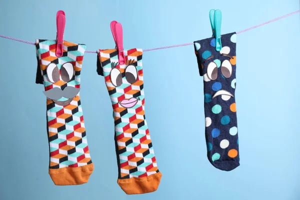 Socks with faces hanging on rope against light blue background. Concept of jealousy