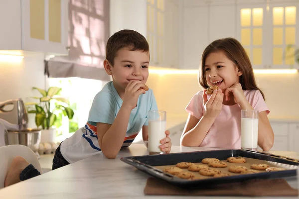 Cute little children eating cookies with milk in kitchen. Cooking pastry