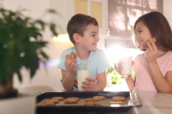 Cute little children eating cookies with milk in kitchen. Cooking pastry