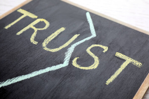 Chalkboard with word TRUST on white table, closeup. Concept of jealousy
