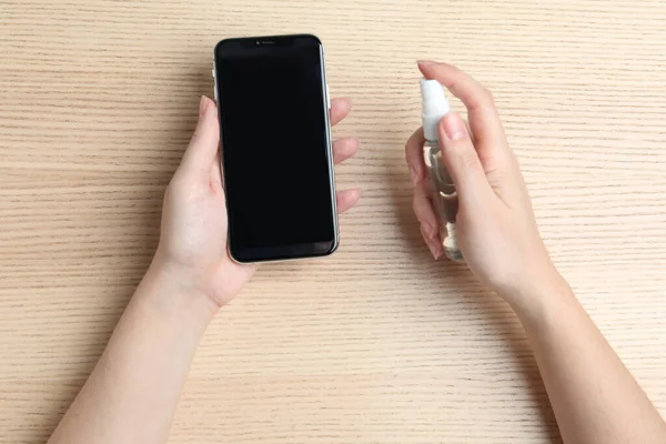 Vrouw Sproeiend Antiseptisch Smartphone Aan Houten Tafel Bovenaanzicht — Stockfoto