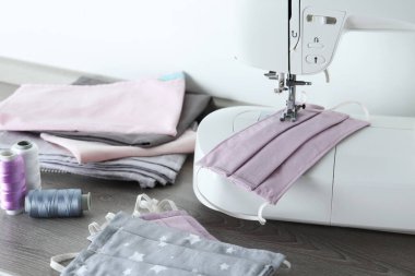 Dikiş makinesi, ev yapımı koruyucu maskeler ve ahşap masadaki iplikler.