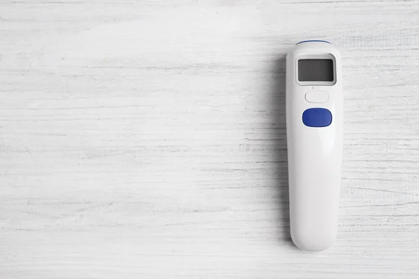 Modern non-contact infrared thermometer on white wooden background, top view. Space for text