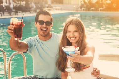 Mutlu genç çift taze yaz kokteylleriyle yüzme havuzunun yanında dinleniyor.