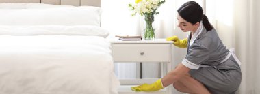 Yatak odasındaki komodinin tozunu silen genç oda hizmetçisi. Pankart tasarımı