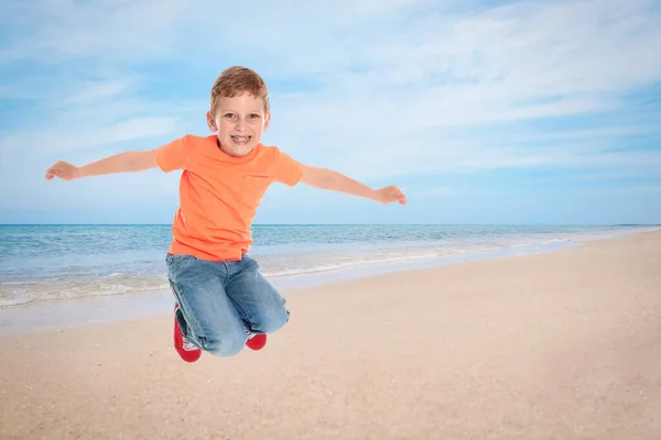Happy school boy jumping on beach near sea. Summer holidays