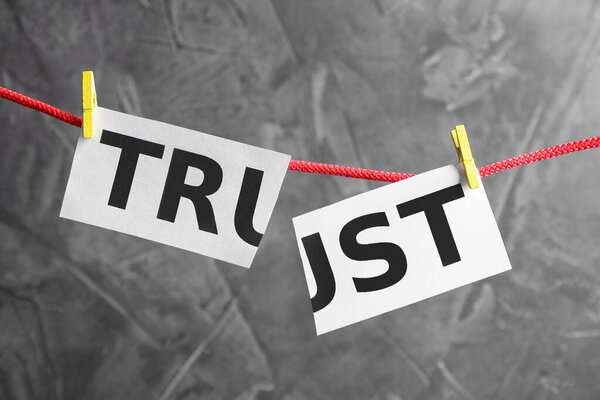 Cut word TRUST hanging on rope against grey background. Concept of jealousy
