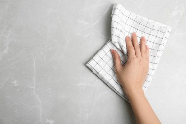Açık gri mermer masayı mutfak havlusuyla silen kadın, üst manzara. Metin için boşluk