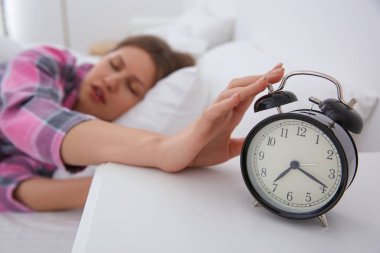 Uykulu genç kadın sabahları evdeki çalar saati kapatıyor, eline odaklanıyor.