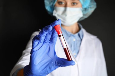 Kan örneğiyle test tüpünü tutan ve siyah arkaplana karşı CORONA VIRUS etiketi takan bilim adamı,
