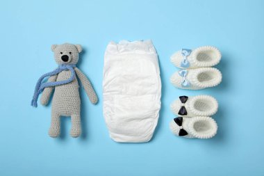 Bebek bezi, oyuncak ayı ve açık mavi arka planda ayakkabılar, düz yatış