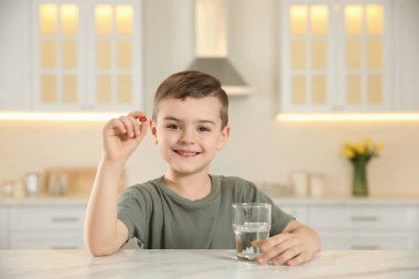 Mutfakta bir bardak su ve vitamin kapsülü olan küçük çocuk.