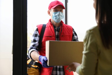 Kurye girişteki kadına karton kutu veriyor. Coronavirus karantinası sırasında teslimat servisi