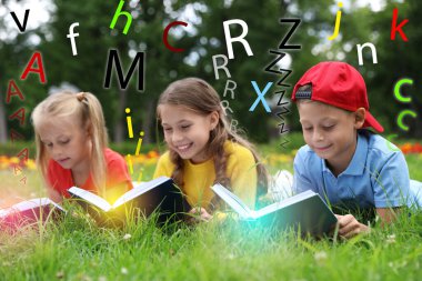 Parkta yeşil çimenler üzerinde kitap okuyan küçük çocuklar grubu