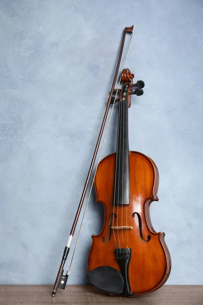 Beautiful violin and bow on wooden table near light blue wall