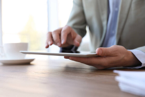 Businessman working with modern tablet at wooden table in office, closeup