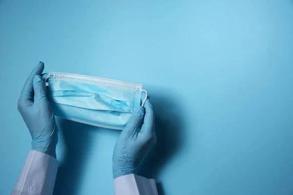 ライトブルーの背景に使い捨てフェイスマスクを保持するラテックス手袋の医師は テキストのためのスペースで閉じます コロナウイルス検疫中の保護処分 — ストック写真