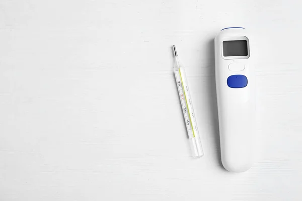 Non-contact infrared and mercury thermometers on white wooden background, flat lay. Space for text