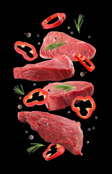 Raw beef meat and other ingredients falling on black background