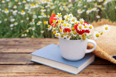 Papatya çayı, haşhaş, hasır şapka ve açık hava masasında kitap kompozisyonu