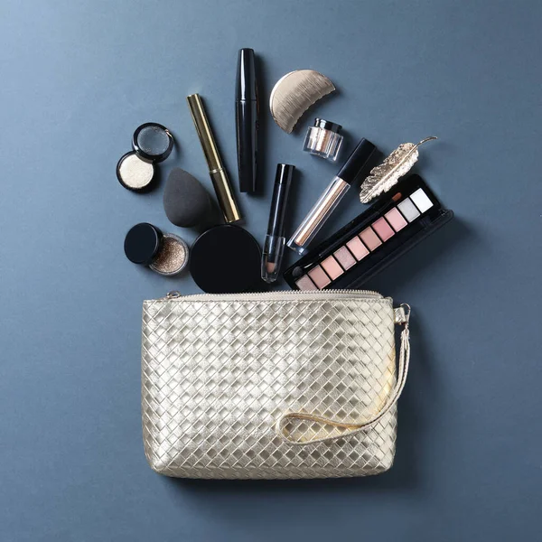 Cosmetic bag with makeup products and beauty accessories on blue-gray background, flat lay