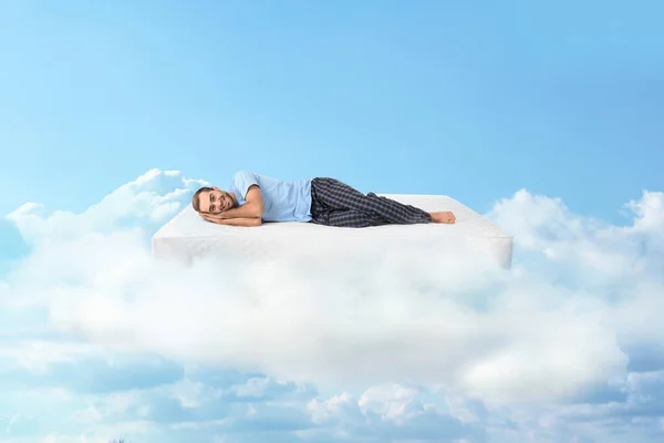 Young man lying on mattress in clouds