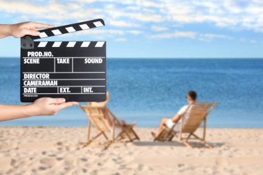 Alkış tahtası tutan asistan ve plajda iskemlede dinlenen insanlar, yakın çekim. Sinema yapımı 