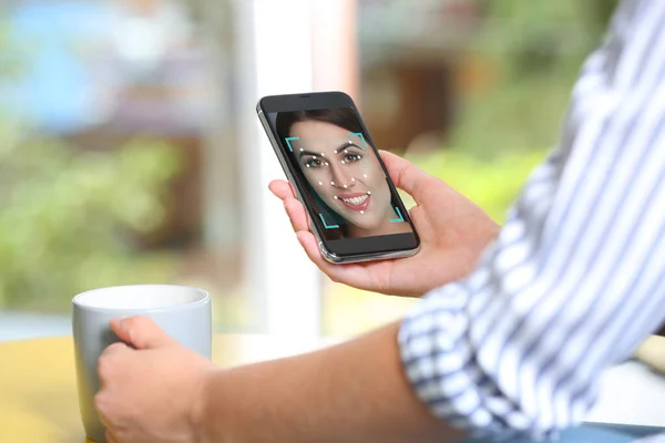 Woman using smartphone with facial recognition system at table indoors, closeup. Biometric verification