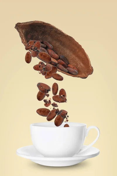 Cocoa pod and beans falling into cup on yellow background