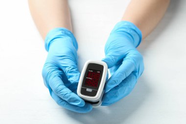 Eldivenli doktor, beyaz ahşap masada nabız oksimetresi tutuyor, yakın plan.