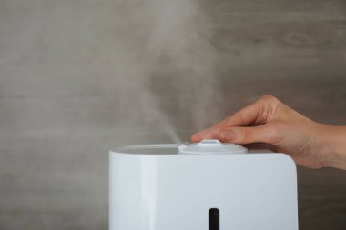 Ahşap arka planda modern hava nemlendiricisi kullanan kadın, yakın plan.