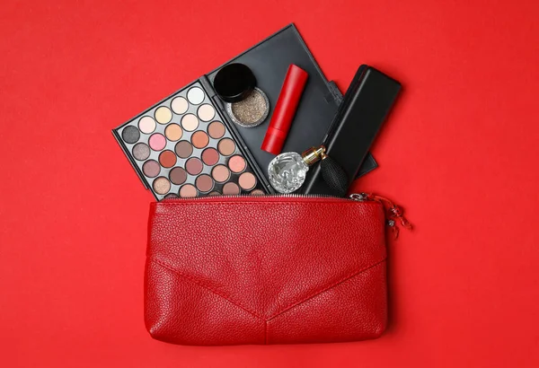 Cosmetic bag with makeup products and perfume on red background, flat lay