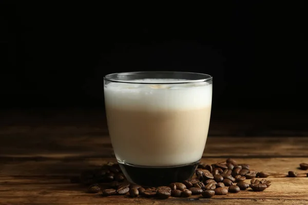 Leckere Latte Macchiato Und Kaffeebohnen Auf Holztisch Vor Schwarzem Hintergrund — Stockfoto