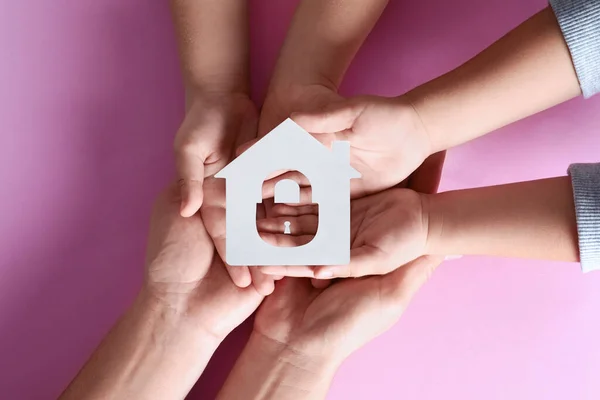 Home security concept. Family holding house on pink background, top view