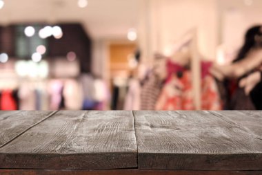 Boş ahşap masa ve modern kıyafetlerle bulanık mağaza manzarası