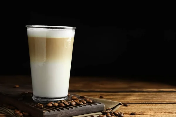 Leckere Latte Macchiato Und Kaffeebohnen Auf Holztisch Vor Schwarzem Hintergrund — Stockfoto