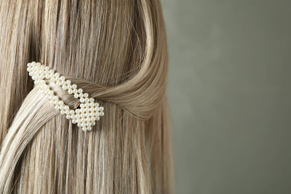 Молодая женщина с красивой заколкой для волос на сером фоне, крупный план

