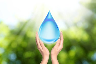 Güneşli yeşil arka planda su damlası ikonu tutan kadın, yakın plan. Ekoloji kavramı