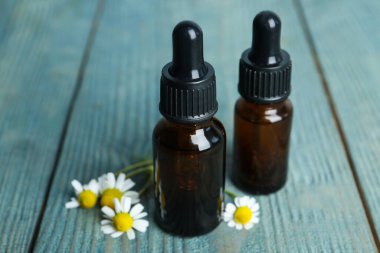 Mavi ahşap masa üzerinde gerekli yağ şişeleri ve taze papatyalar.