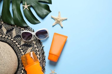 Açık mavi zemin üzerinde güneş koruma ürünleri ve plaj aksesuarları bulunan düz bir bileşim. Metin için boşluk