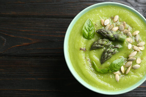Delicious asparagus soup in bowl on black wooden table, top view. Space for text
