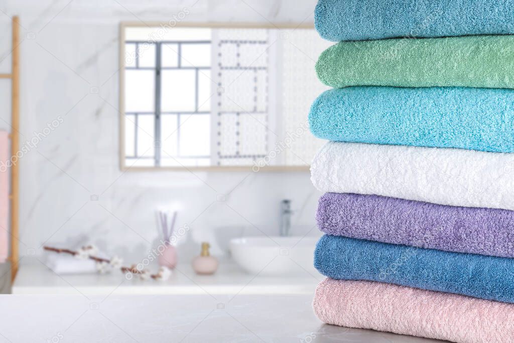 Stack of fresh towels on light grey table in bathroom. Space for text