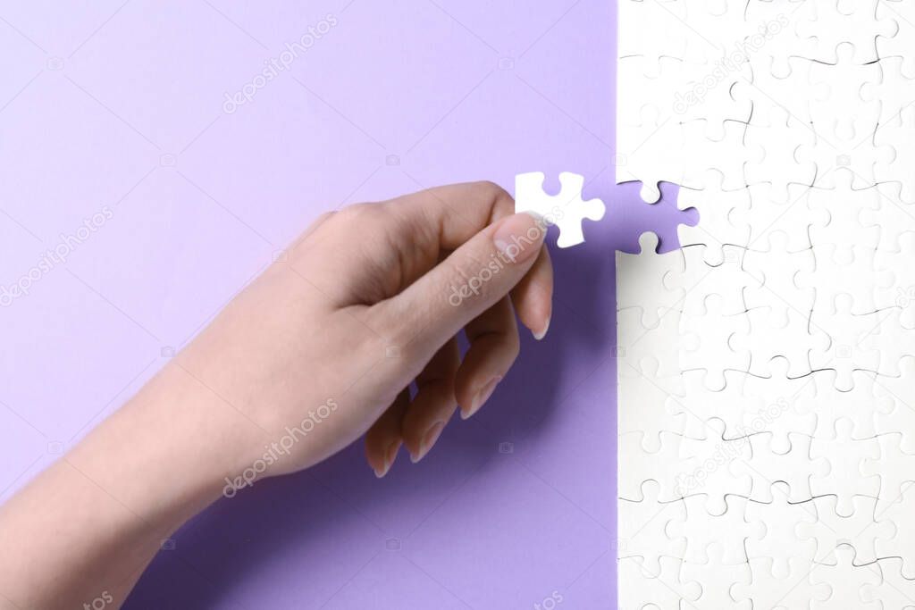 Woman putting last piece of white puzzle on violet background, closeup