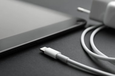 Tablet ve USB kablosu siyah arkaplanda, yakın plan. Modern teknoloji