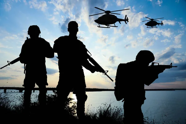 屋外でパトロールしているアサルトライフルと軍用ヘリコプターと一様に兵士のシルエット — ストック写真