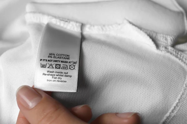 Kobieta Czytająca Etykietę Odzieży Symbolami Pielęgnacji Zawartością Materiału Białej Koszuli — Zdjęcie stockowe