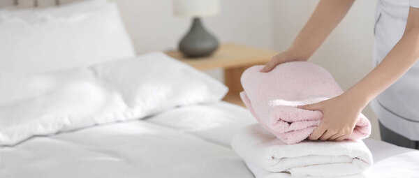 Молодая горничная кладет стопку свежих полотенец на кровать в гостиничном номере, вид крупным планом с пространством для текста. Баннерный дизайн
