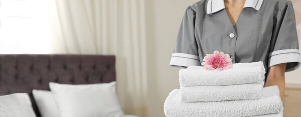 Chambermaid holding stack of fresh towels in hotel room, closeup view with space for text. Banner design