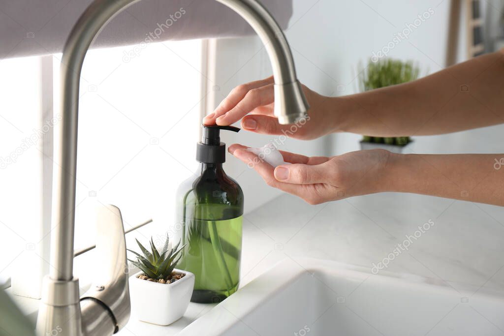Woman using soap dispenser in kitchen, closeup